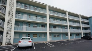 Un edificio de varios pisos con balcones, un estacionamiento y un coche blanco estacionado al frente.