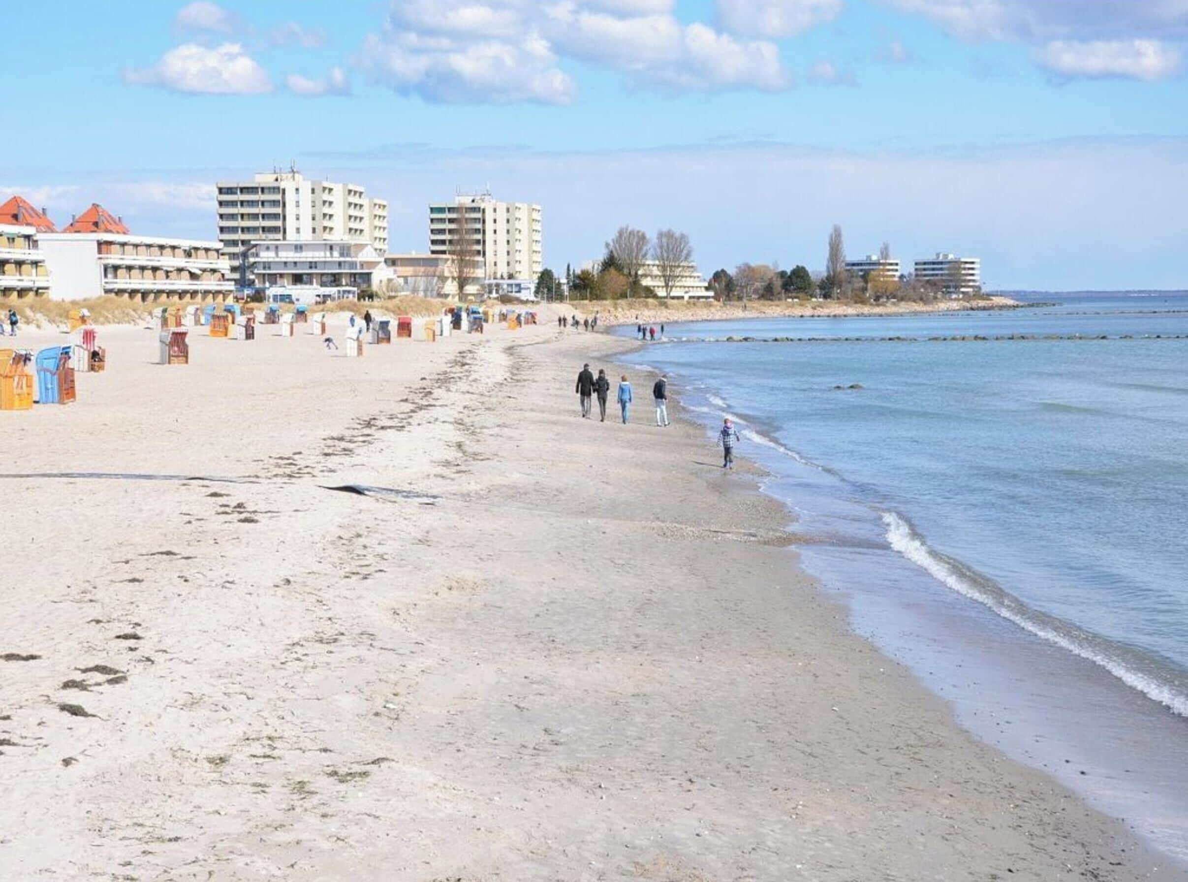 A beach with a sandy shore, a few people walking, and buildings in the background.