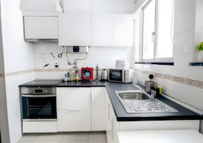 A modern kitchen with white cabinets, a black countertop, a red appliance, a microwave, a kettle, and a sink. - Apartment 'Reis Turismo' with Balcony, Wi-Fi and Air Conditioning (Faro)
