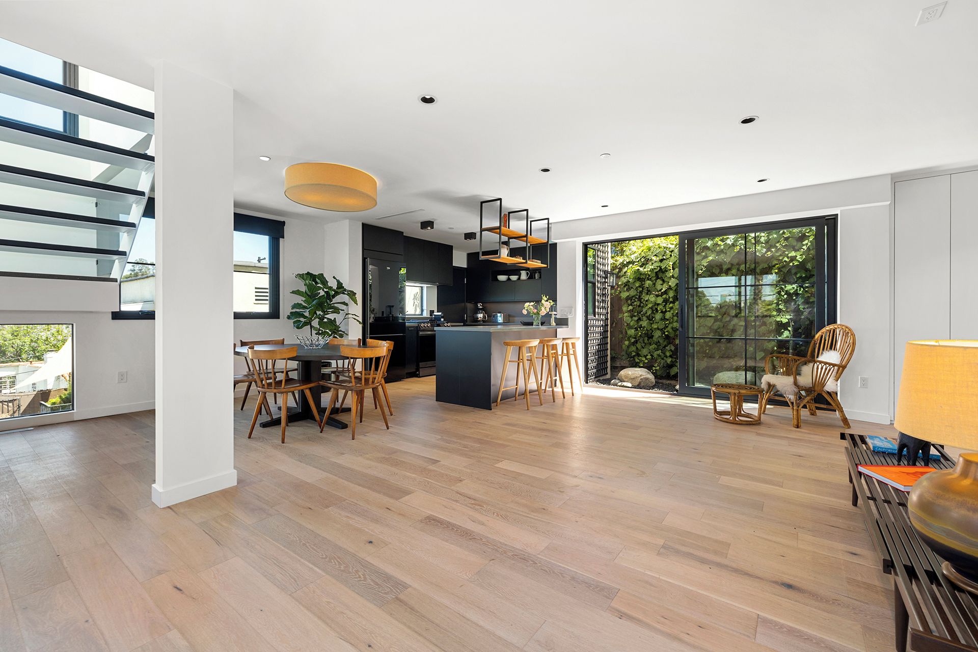 A modern kitchen with a central island, a dining area with wooden chairs, and large sliding glass doors leading to a garden.