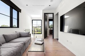 A modern living room with a sofa, a coffee table, and a TV. There is a view of the outdoors through large windows. - Peaceful & Cozy 2 Bedroom House, Stunning Views (Los Angeles)