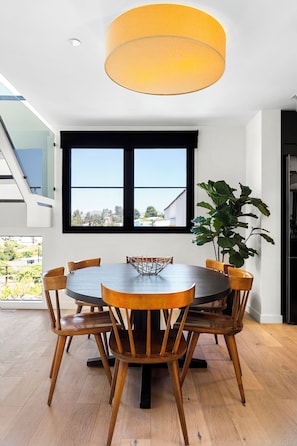 Un coin repas avec une table ronde, des chaises en bois et une grande fenêtre donnant sur des bâtiments et de la verdure.