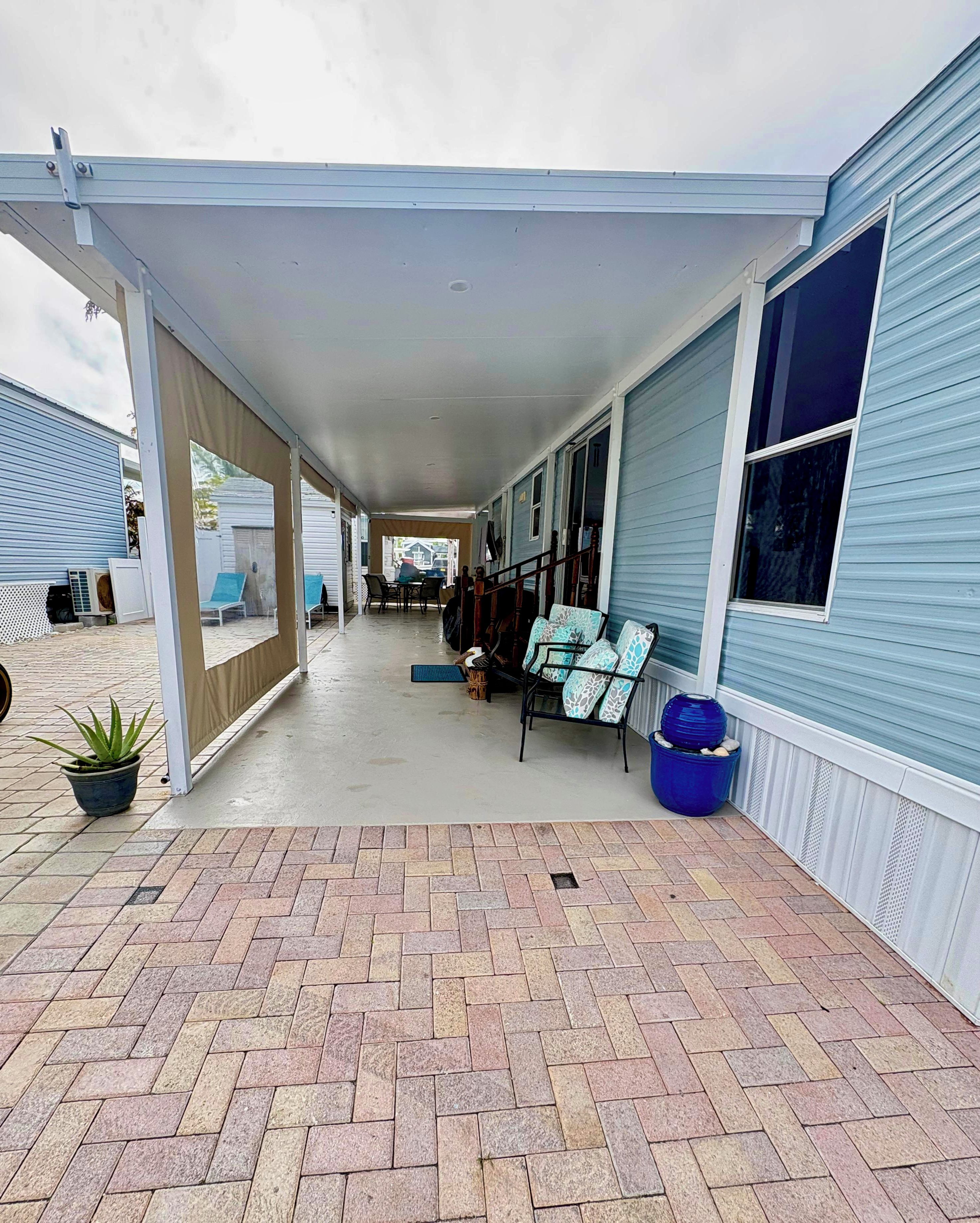 A covered patio area with a brick floor, outdoor seating, and a covered walkway leading to a building.