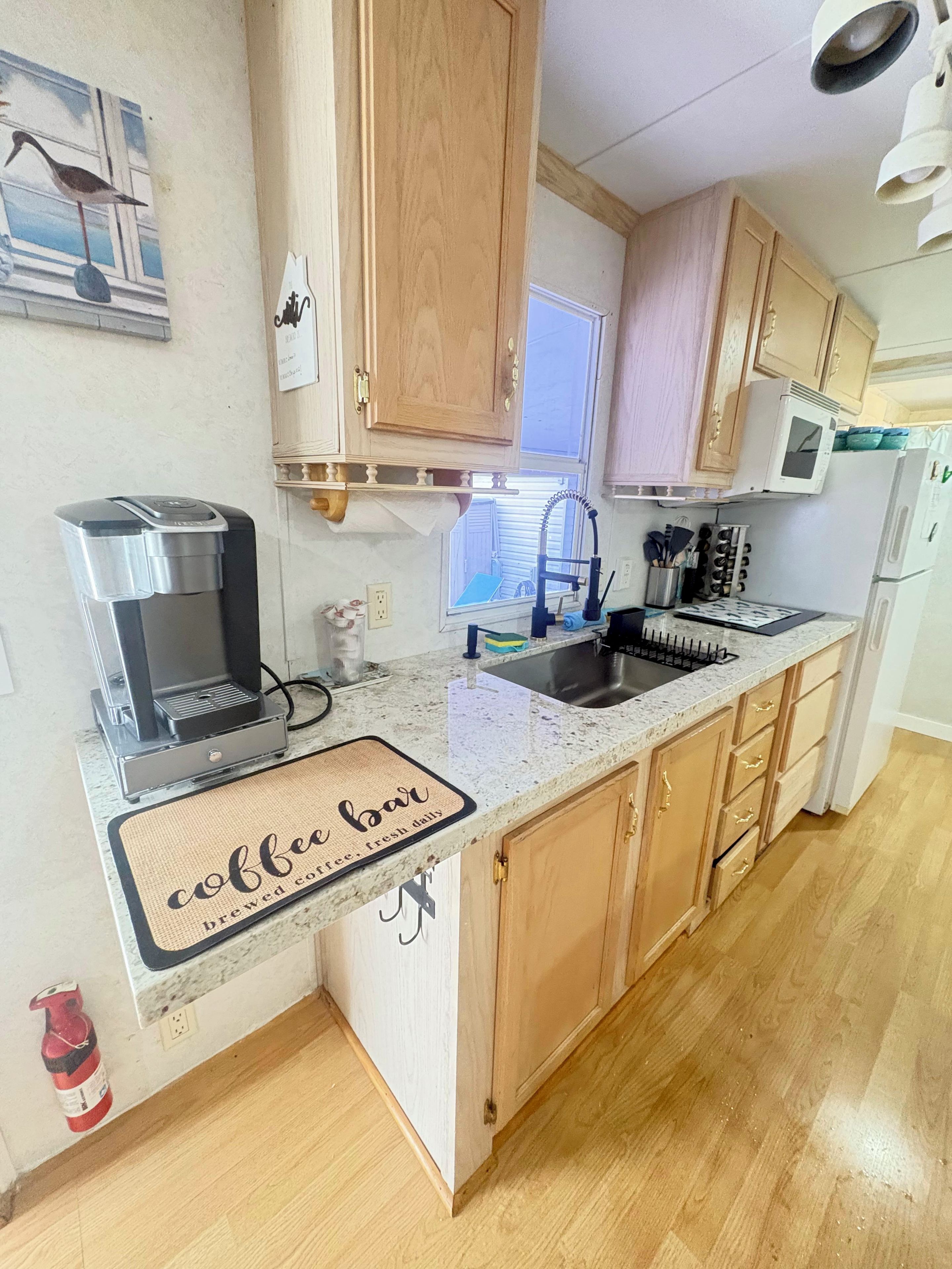 A kitchen with wooden cabinets, a coffee machine, a sink, and a window.