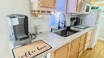 A kitchen with wooden cabinets, a coffee machine, a sink, and a window.