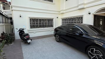 Un immeuble de deux étages avec un garage, une voiture noire garée et un scooter.