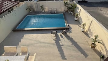 A rooftop swimming pool with lounge chairs and potted plants.