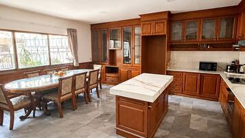 A spacious kitchen with a marble island, wooden cabinets, and a dining area with a glass-top table and chairs.
