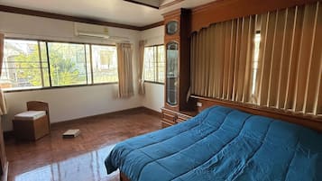 A bedroom with a wooden bed, a nightstand, a dresser, a window with curtains, and an air conditioning unit.
