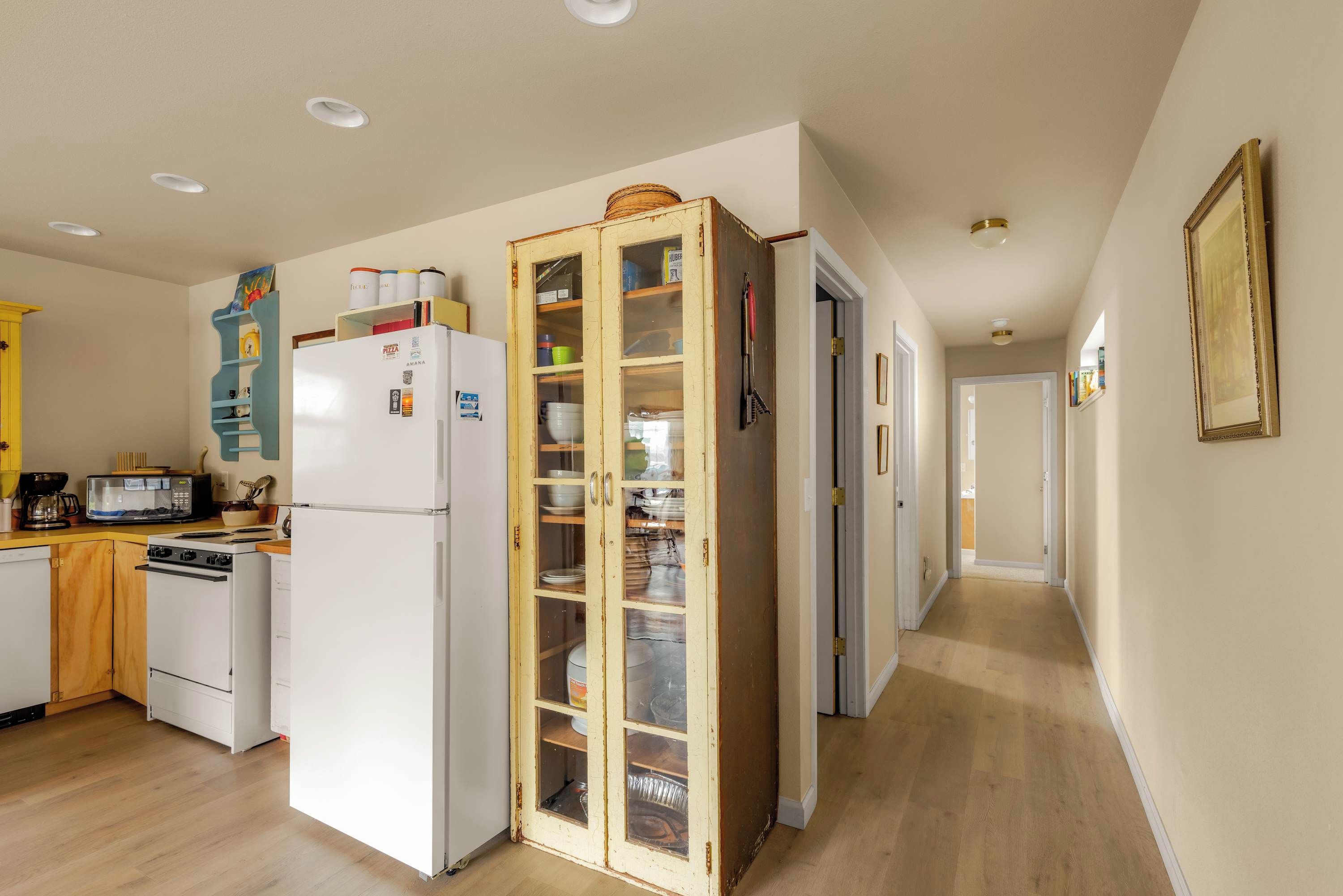 A kitchen with a refrigerator, microwave, and stove. There is a wooden cabinet with glass doors containing dishes.