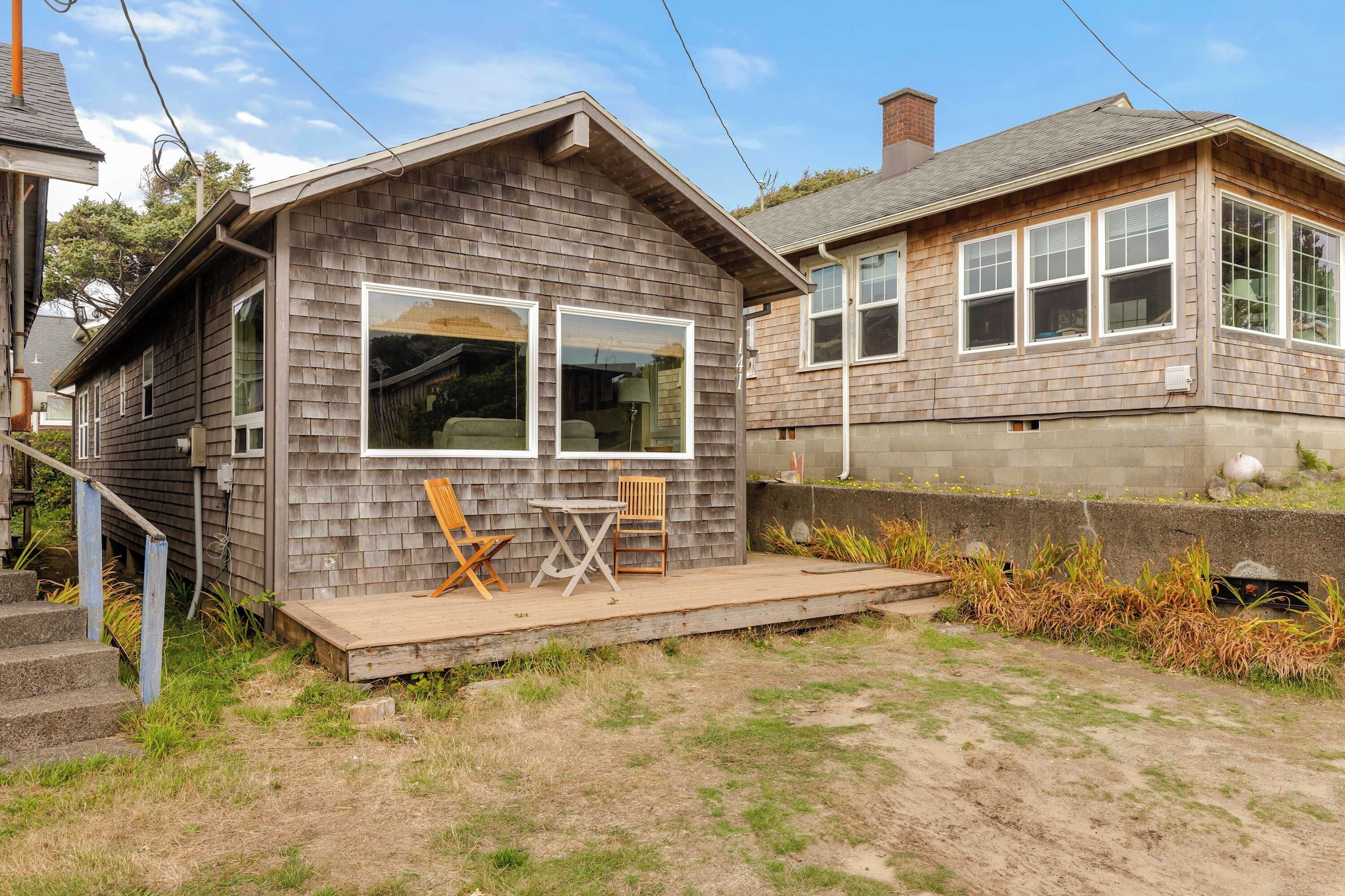 A small wooden cabin with a porch, two chairs, and a table.