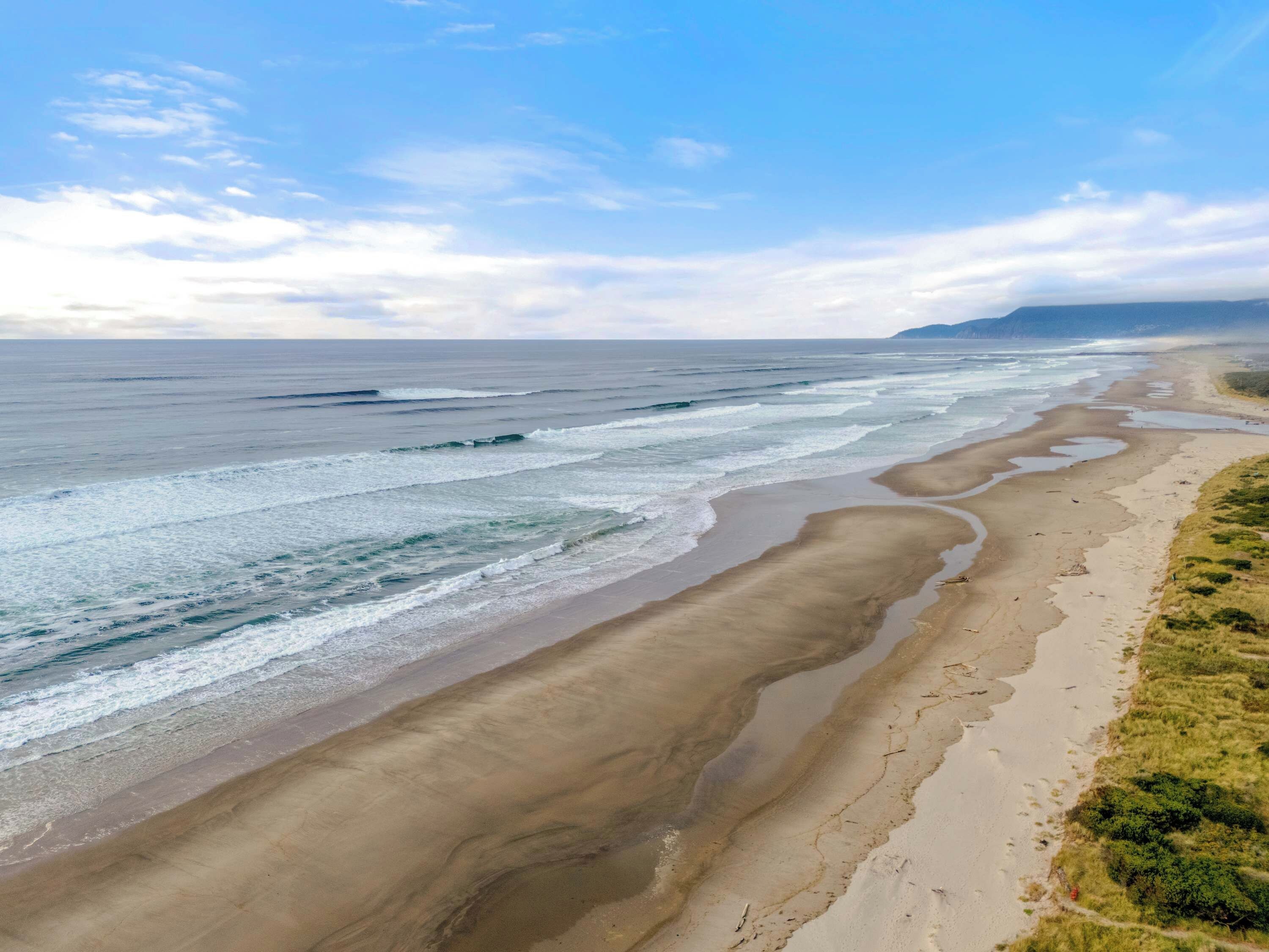 A coastal beach with waves, a sandy shore, and distant land.
