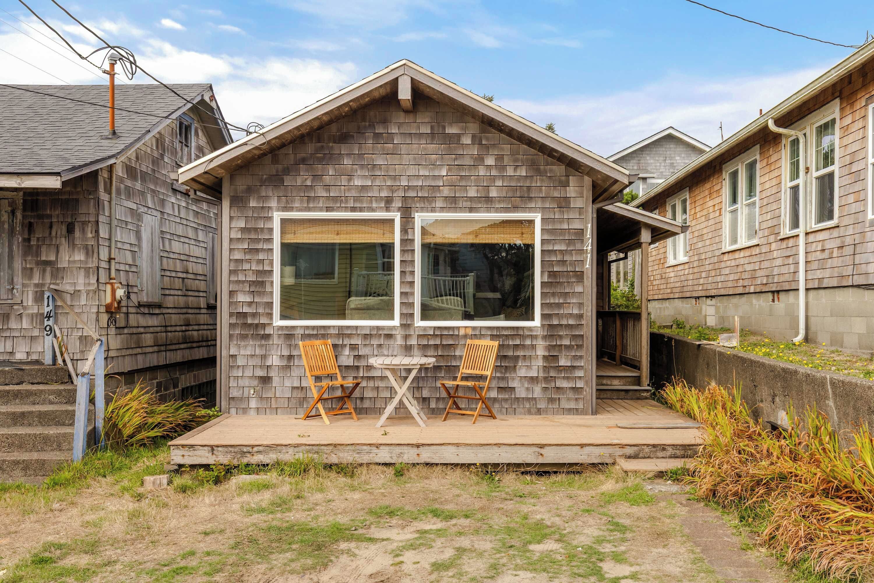 A small wooden house with a porch, two wooden chairs, and a table.