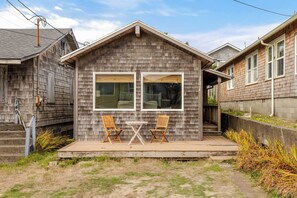 A small wooden house with a porch, two wooden chairs, and a table.