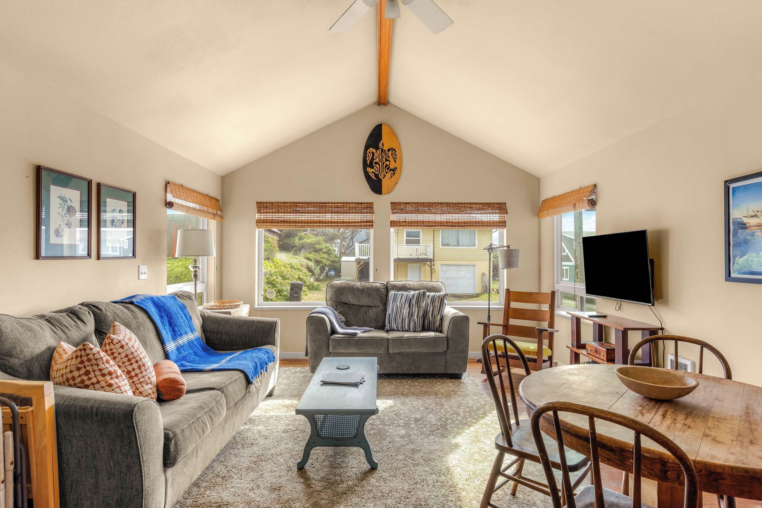 A cozy living room with a high ceiling, a large window, and a flat-screen TV.