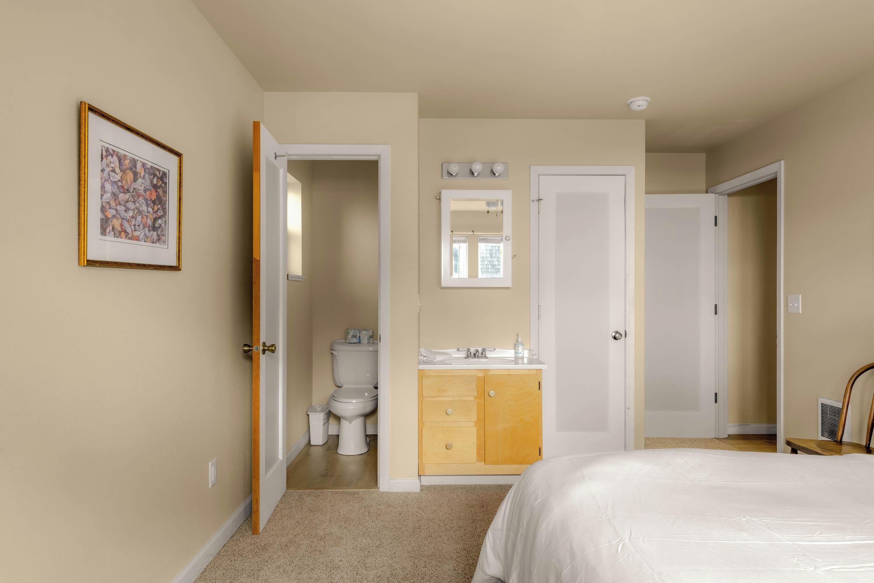Ein Schlafzimmer mit Bett, ein Badezimmer mit Toilette, Waschbecken und Spiegel, sowie ein Flur, der zu einem weiteren Raum führt.