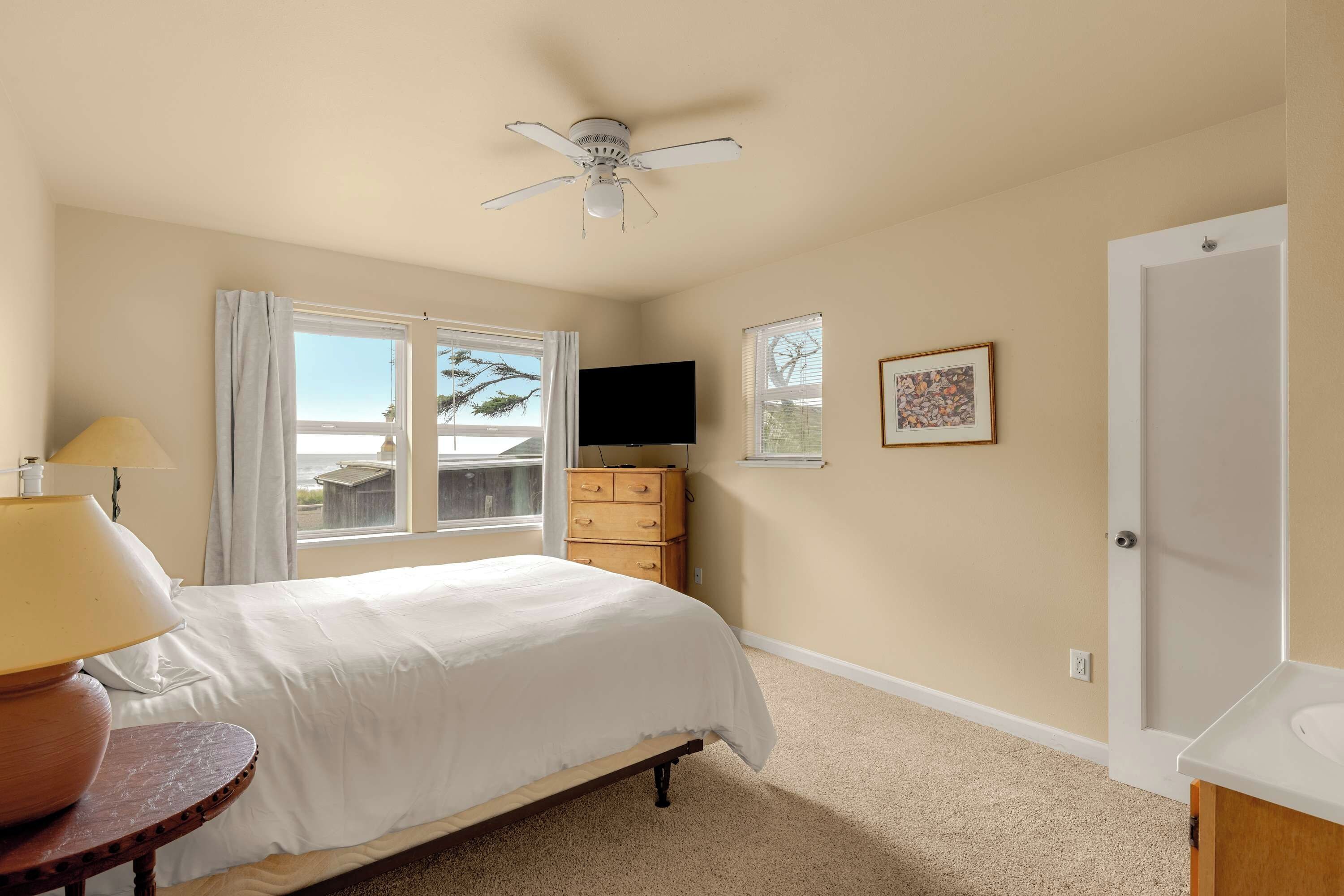 A bedroom with a bed, a ceiling fan, a dresser, a TV, and a door.