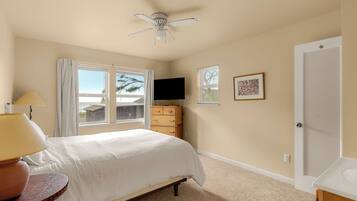 A bedroom with a bed, a ceiling fan, a dresser, a TV, and a door.