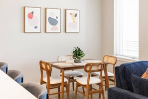 Un coin repas avec une table en bois, quatre chaises et trois tableaux abstraits encadrés accrochés au mur.