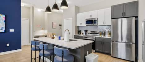 A modern kitchen with a central island, bar stools, stainless steel appliances, and pendant lighting.