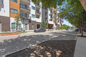 A multi-story residential building with balconies, a paved street, and a car parked on the side. - Luxe 2BR Downtown Fort Worth; Balcony, Sleeps 6 ; Near Sundance Sq & Dickies (Fort Worth)