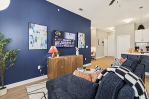 Un salon moderne avec un mur d’accent bleu foncé, un téléviseur fixé au mur et une console en bois.