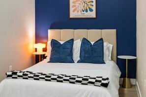 Een hotelkamer met een bed, twee bedlampen, een blauwe muur en een lijst met kunstwerk erboven.