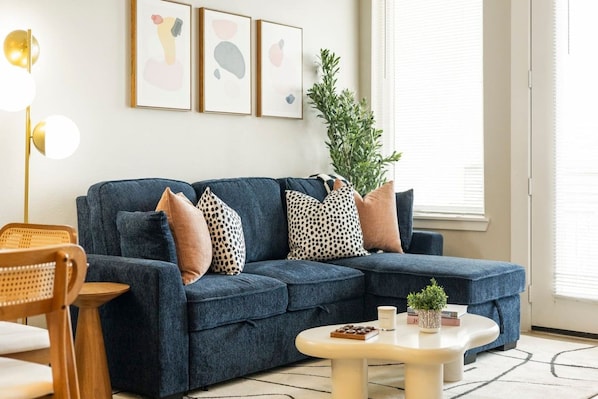 A living room with a blue sofa, a round coffee table, and a plant. - Chic 1BR Downtown Fort Worth ; Sleeps 4 ; Near Sundance & Dickies (Fort Worth)
