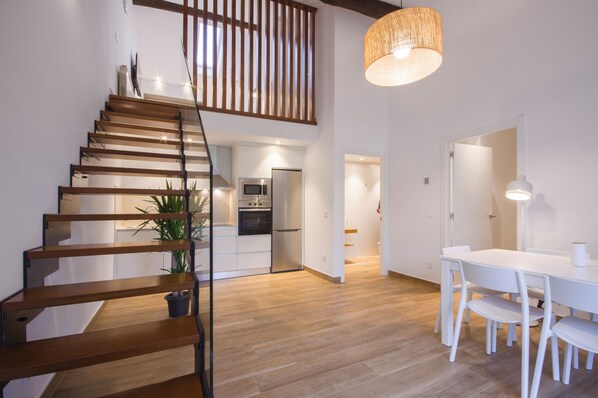 A modern interior with a wooden staircase, a dining area with white furniture, and a kitchen with stainless steel appliances. - TWO-BEDROOM APARTMENT (castroverde)