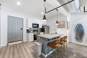 Een moderne keuken met een centraal eiland, barstoelen en roestvrijstalen apparatuur.