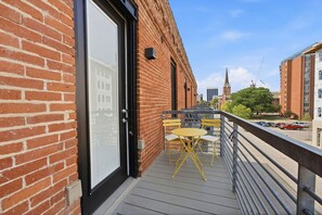 Ein Balkon mit Tisch und Stühlen, ein Backsteinhaus und ein Blick auf ein Kirchturm in der Ferne.