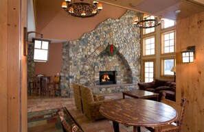 A stone fireplace with a fire, wooden furniture, and large windows. - Prime River Run Village Location | Walk to Gondola (Keystone)