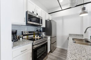 A modern kitchen with white cabinets, stainless steel appliances, a granite countertop, and a built-in oven. - Luxury Studio Living: Sleeps 2; Heart of Columbus (Columbus)