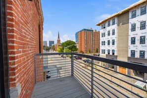 A balcony with a metal railing overlooking a street with cars and buildings, including a church spire in the distance. - Luxury Studio Living: Sleeps 2; Heart of Columbus (Columbus)