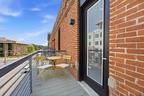 A balcony with a table and chairs, a brick wall, and a large window. - Luxury Studio Living: Sleeps 2; Heart of Columbus (Columbus)