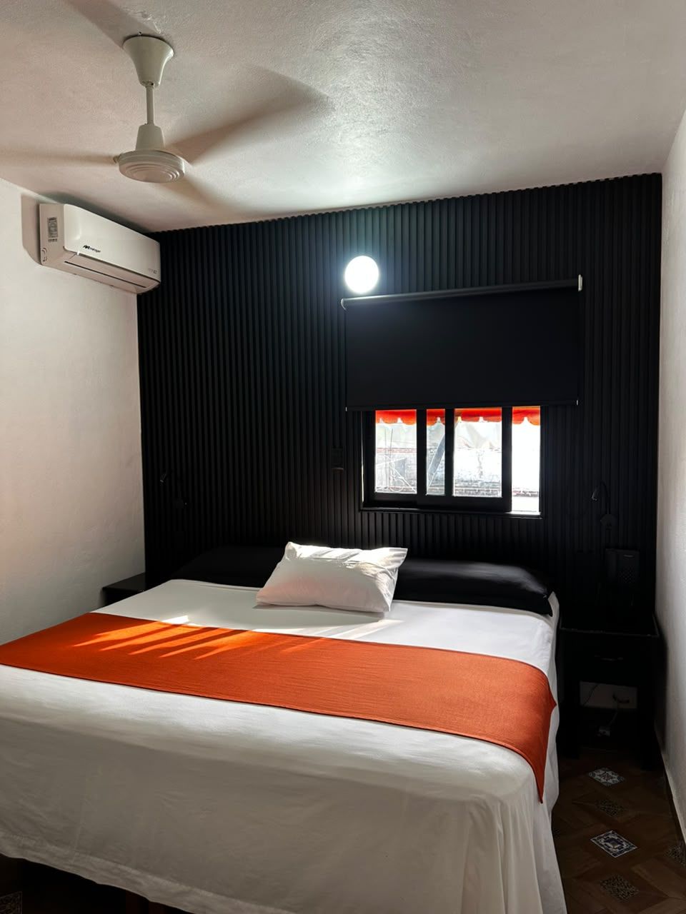 Un dormitorio con cama, ventilador de techo, equipo de aire acondicionado y ventana con persianas.