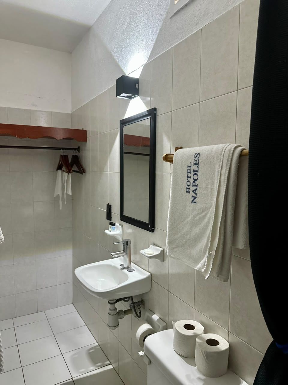 Un baño con lavamanos, espejo, toallero y papel higiénico.