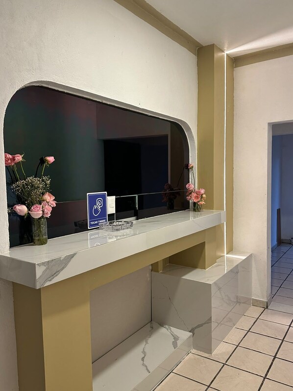 A reception desk with a marble top, a blue sign with accessibility symbols, and pink flowers in vases.
