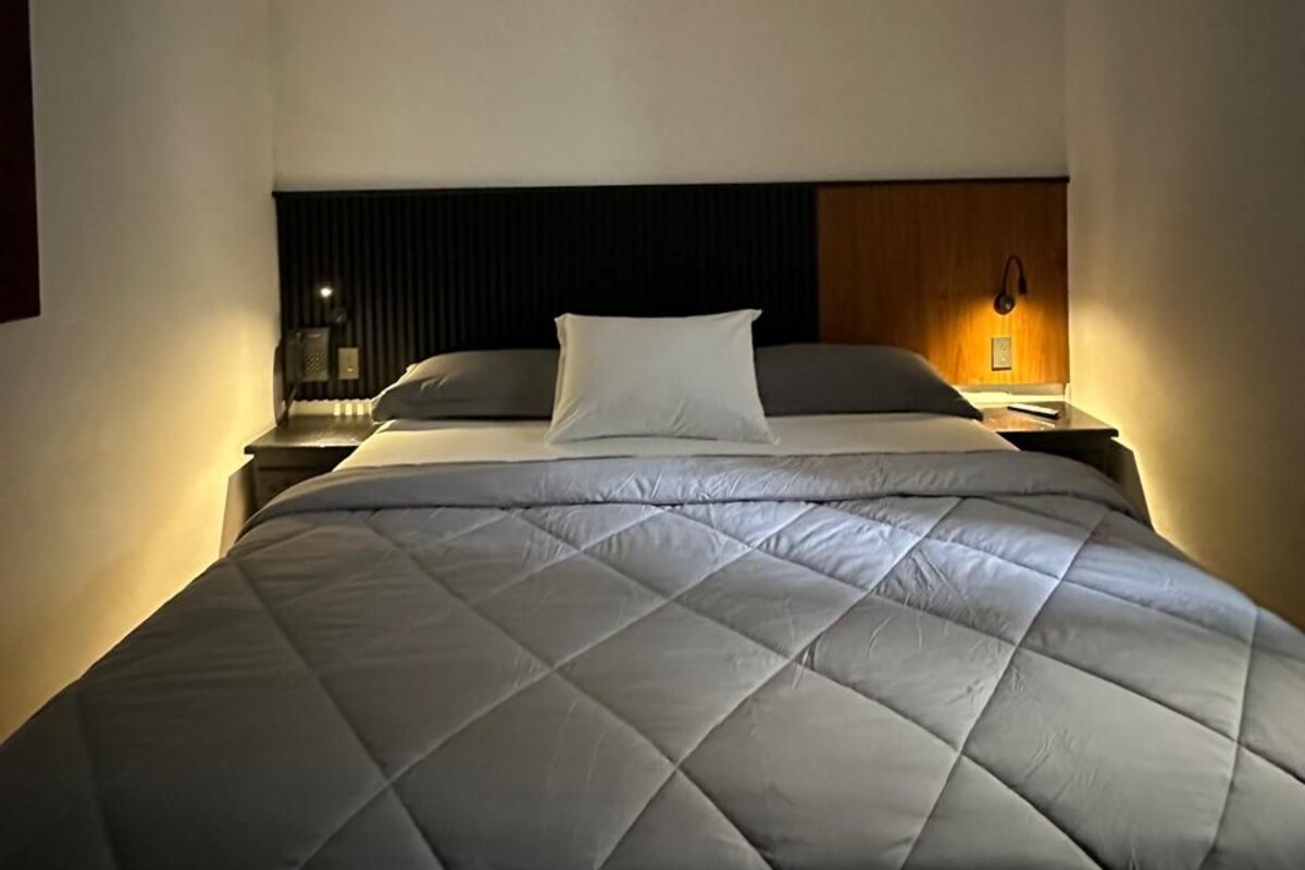 A hotel room with a bed, a nightstand, a wall clock, and a ceiling fan.