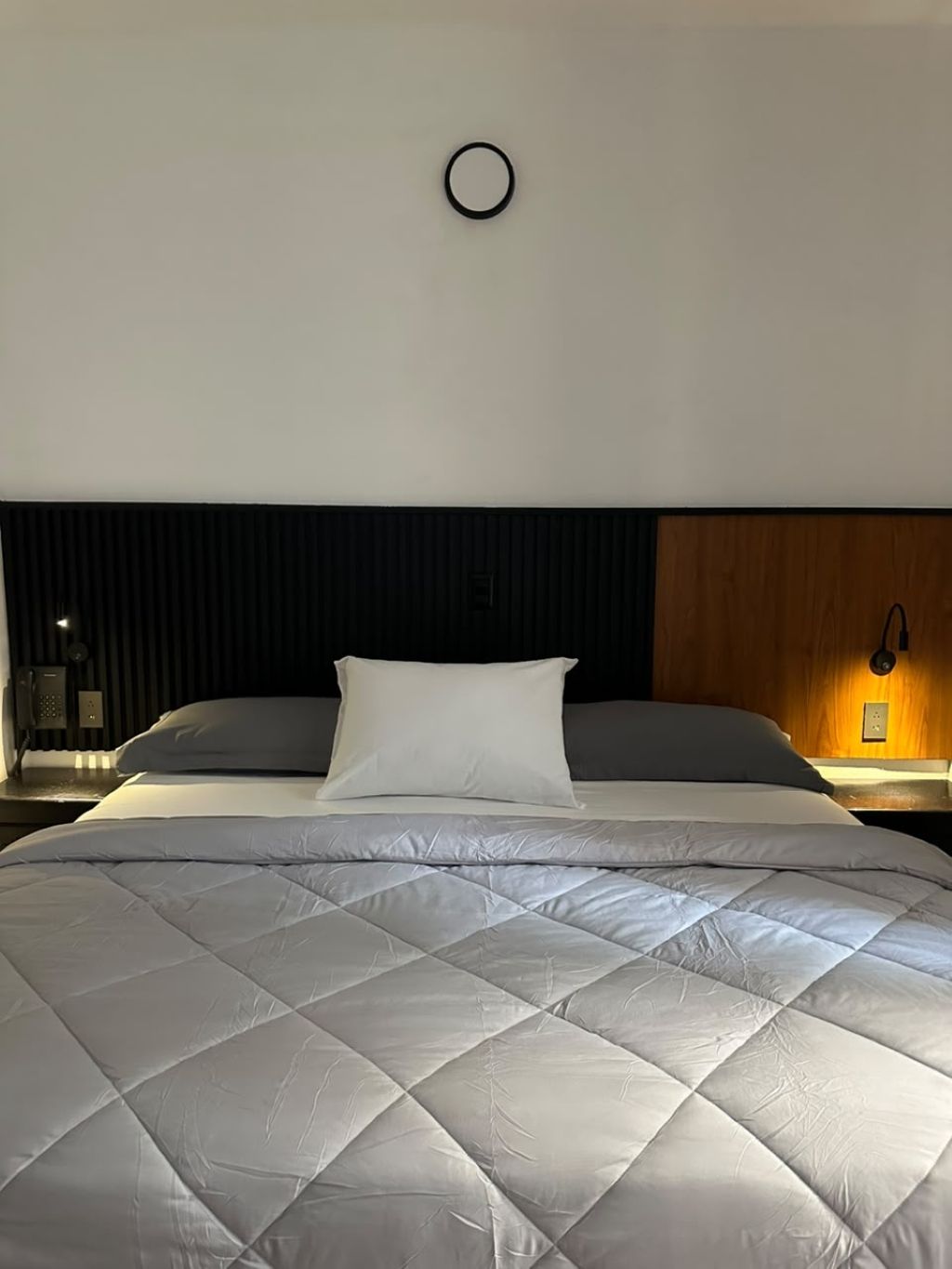Ett hotellrum med en säng, ett nattduksbord, en vägglampa och en träpanel på väggen.