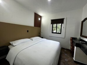 A bedroom with a bed, a nightstand, a desk, a mirror, and a window. - Hotel Nápoles (El Trapiche)