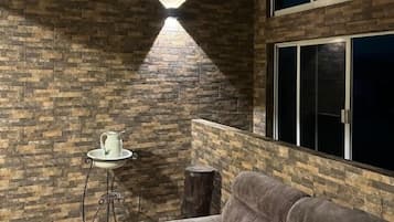 A room with a brick wall, a window, a sofa, a small table with a pitcher, and a hanging light fixture.