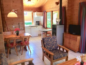 A cozy cabin interior with a dining area, kitchen, and a living room with a television.