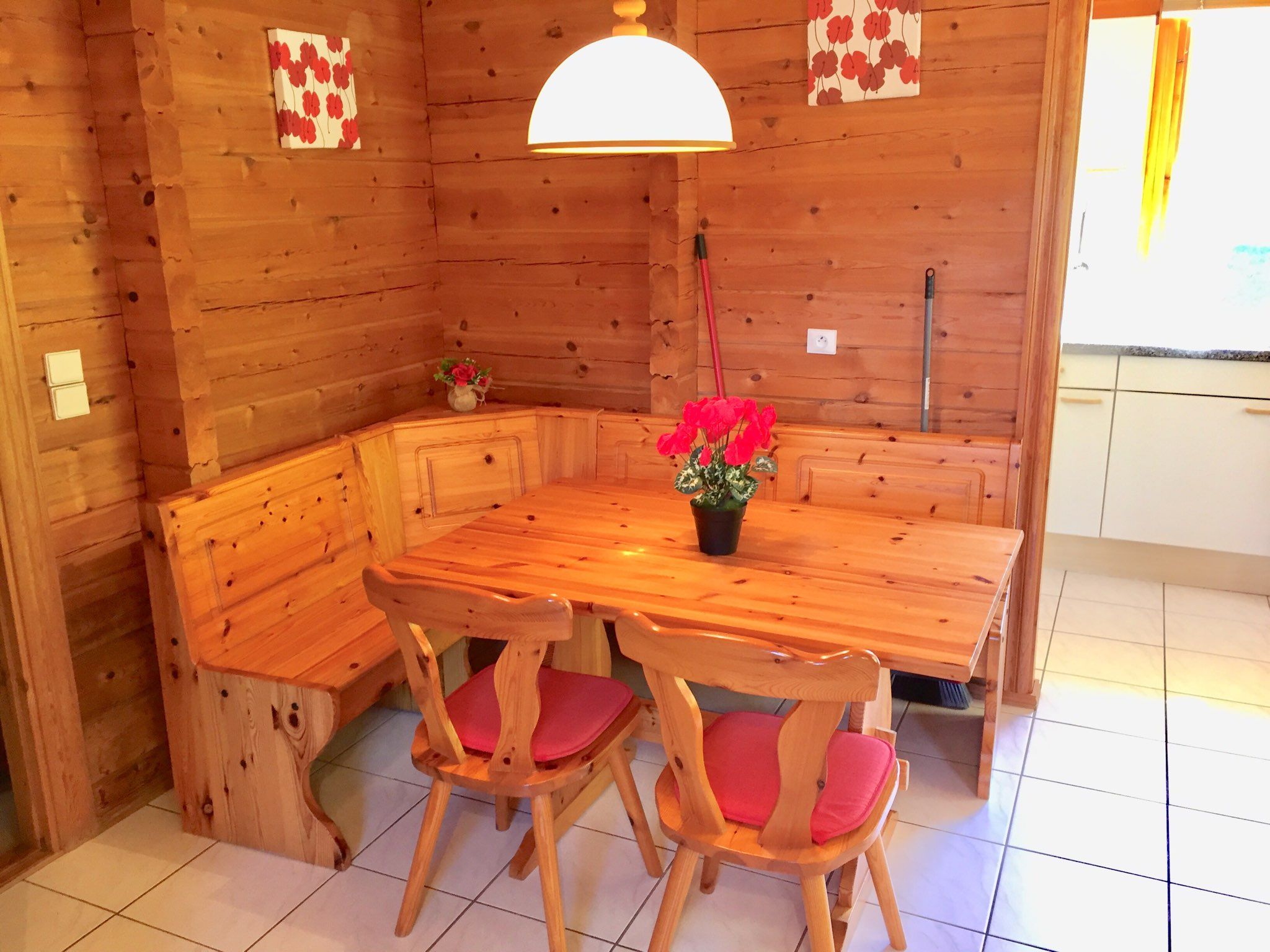 Un intérieur en bois avec une table ronde et des chaises, un luminaire suspendu et un petit vase avec des fleurs.