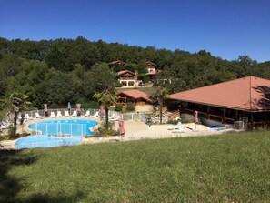 A resort with a swimming pool, lounge chairs, and a building with a red roof.