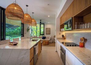 A modern kitchen with a marble countertop, wooden cabinets, and pendant lighting. - Seasons at Ceiba | Staffed Luxury House + Gym (Pinilla)