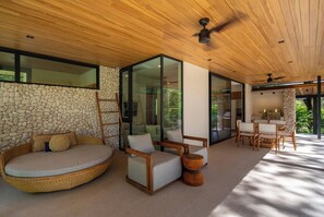 A modern interior with a stone wall, a round wicker sofa, and a dining area with wooden furniture. - Seasons at Ceiba | Staffed Luxury House + Gym (Pinilla)