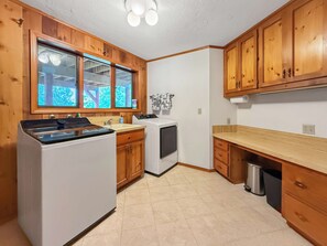 A kitchen with wooden cabinets, a stove, a washing machine, and a window with a view of trees. - Modern 3BR Retreat with Sauna & Hot Tub Sleeps 8 (Sequim)