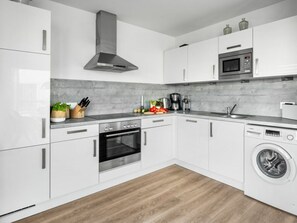 A modern kitchen with white cabinets, a stainless steel range hood, a built-in oven, a microwave, and a front-loading washing machine. - Holiday Apartment With 1 Bedroom (Kappeln)