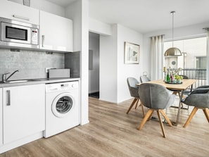 A modern kitchen with a built-in washing machine, a microwave, and a dining area with a table and chairs. - Holiday Apartment With 1 Bedroom (Kappeln)